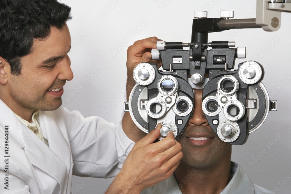 Mature male optometrist adjusting panels of phoropter while examining patient