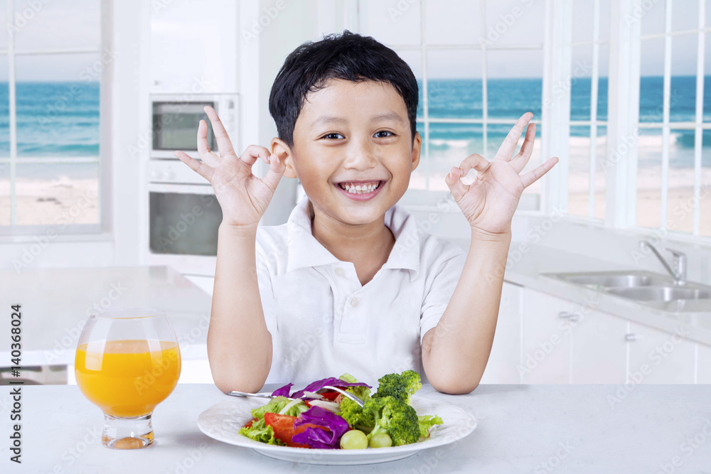 Happy little boy with salad in the kitchen