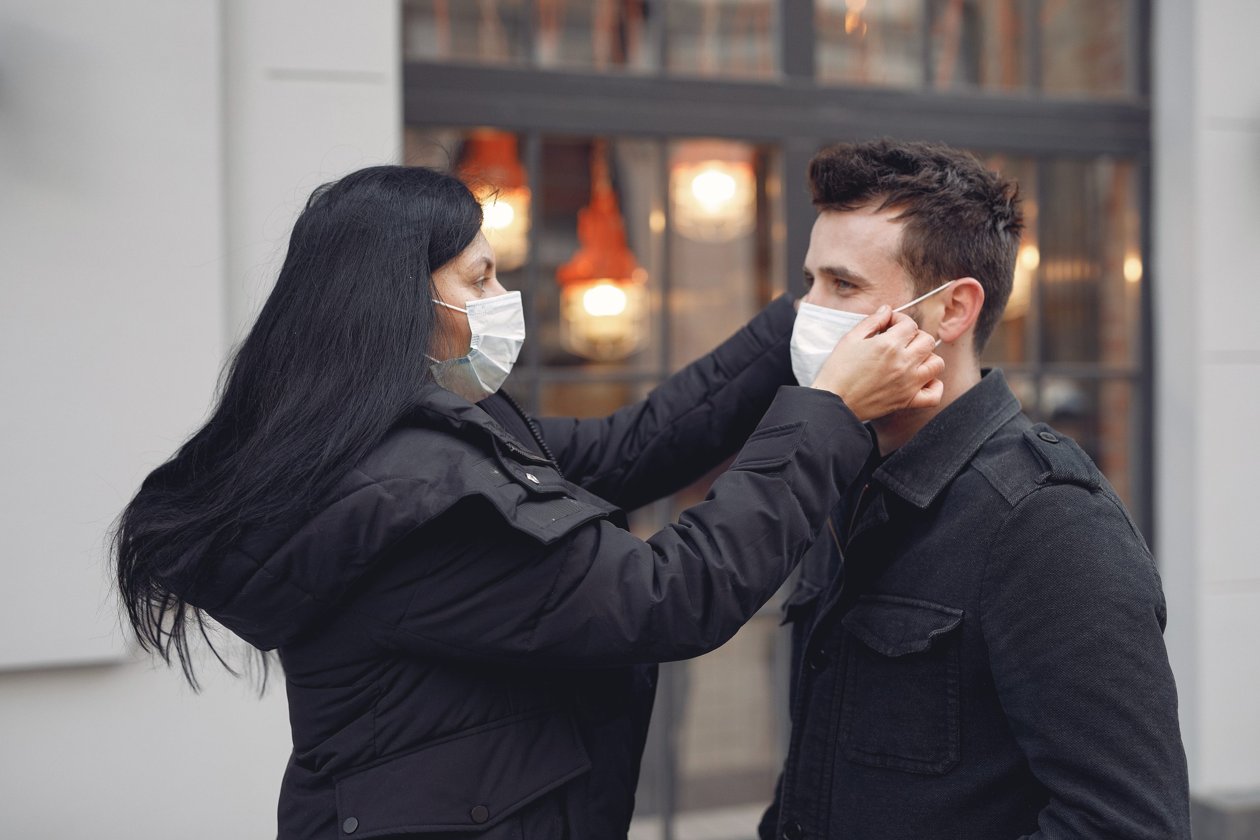 Young careful couple adjusting medical masks against urban building